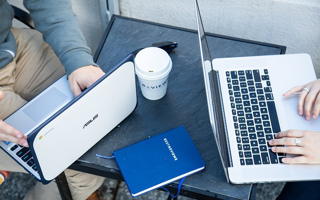 Two people at a table typing on laptops